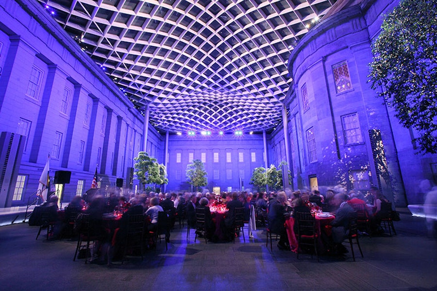 attendees seated at an event in the Kogod Courtyard illuminated at night with  grand architecture 