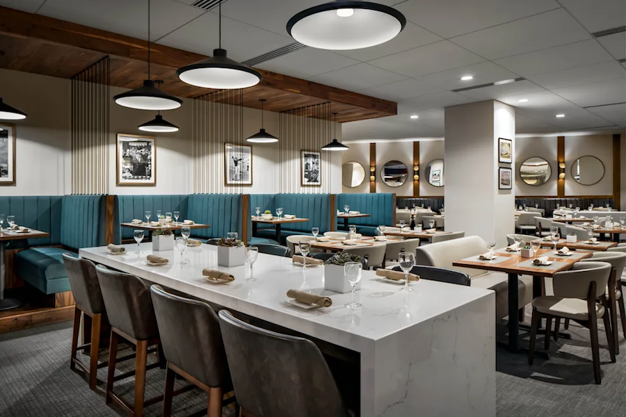 sleek restaurant interior with a white marble countertop in the foreground and other tables and teal blue booth in the background