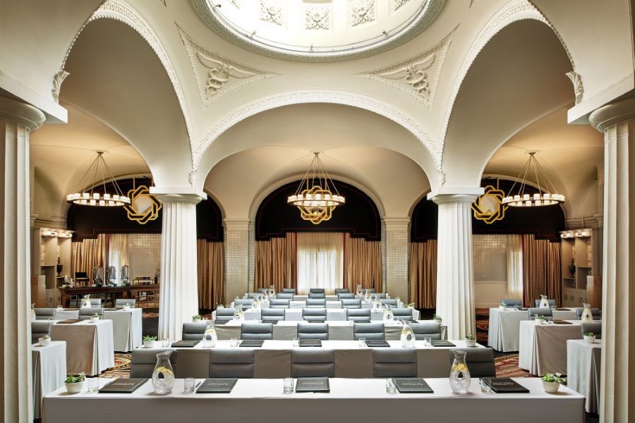 A grand, elegant ballroom at the Monaco featuring high arched ceilings, ornate chandeliers, and a sophisticated classroom-style setup with plush seating and classic decor.