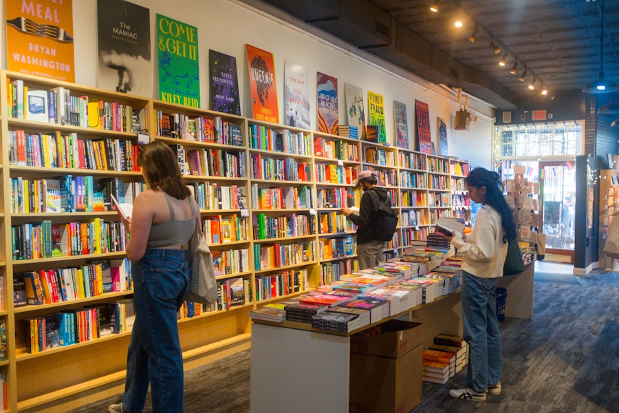  Customers browse books in a brightly lit bookstore, with shelves full of colorful titles and posters on the walls above.