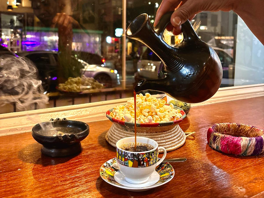 A traditional Ethiopian coffee is poured into a decorative cup, accompanied by incense and a bowl of popcorn.