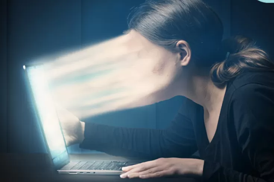 A surreal image of a person sitting in front of a laptop, with their face stretched into the screen by bright light beams, symbolizing the overwhelming or absorbing nature of digital media.