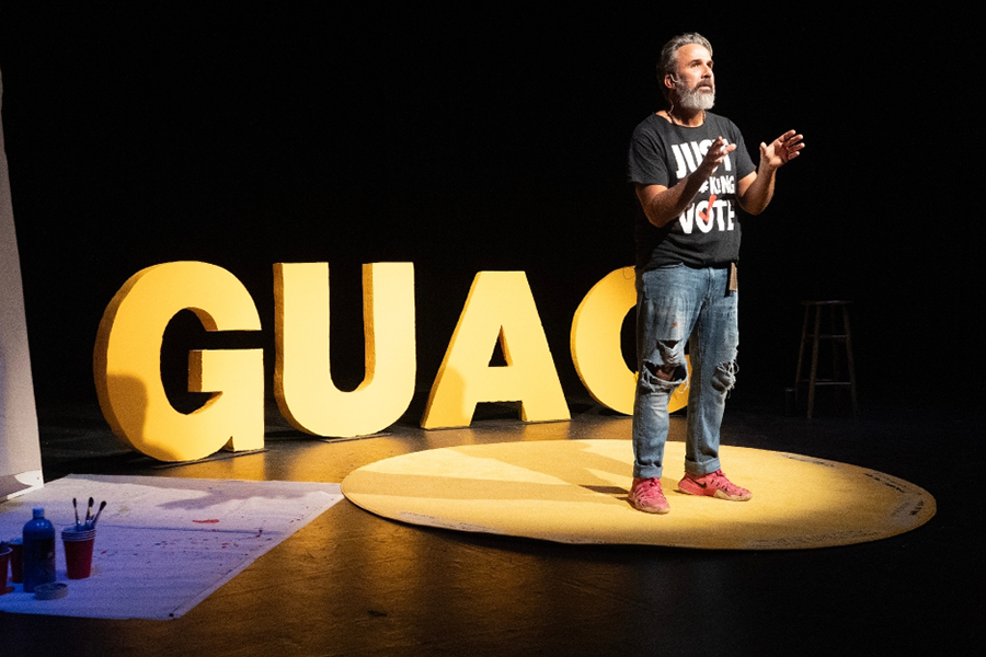 Person standing on stage in front of "Guac"