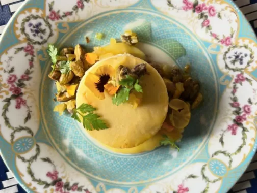 Close-up of a beautifully plated cheesecake with pistachios and edible flowers on an ornate blue and white dish